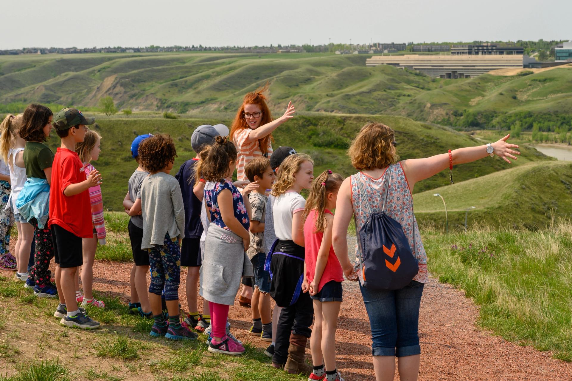 Group of children and adults standing on hillside trail overlooking green rolling valley.