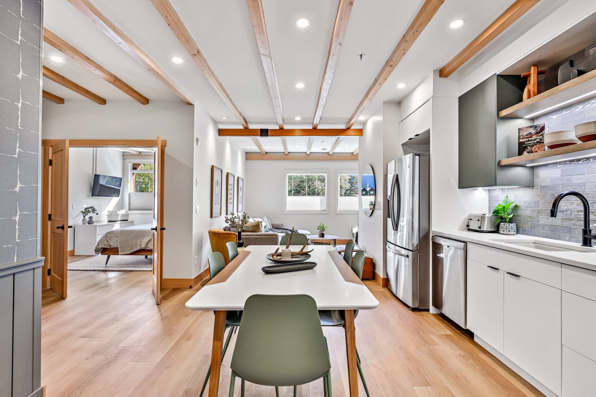 Modern kitchen and dining area with wood beams, white cabinets, and bright natural light.