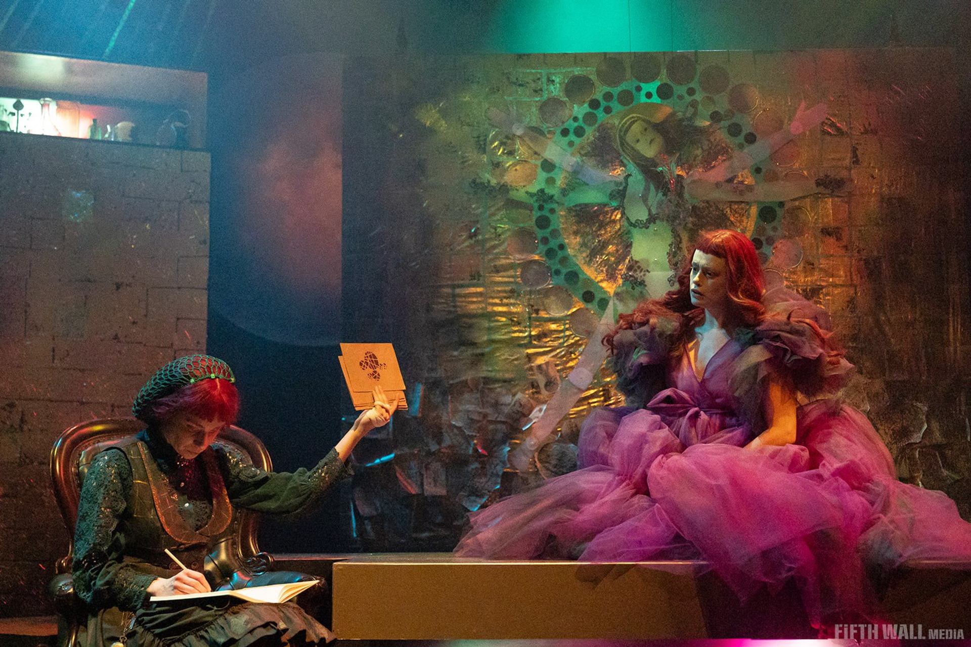Theatre scene with two performers, one sketching, one in voluminous pink gown.