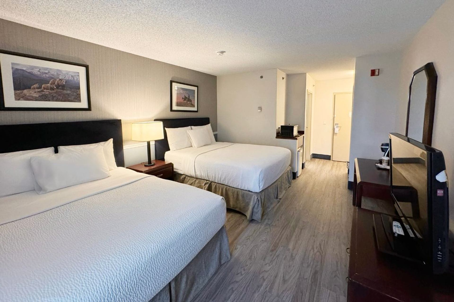 A guest room features two queen beds, wood flooring, modern furnishings, and soft ambient lighting.