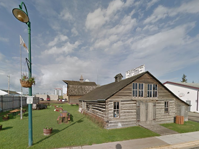 Weathered log cabin with pitched roof and museum sign on grassy lot