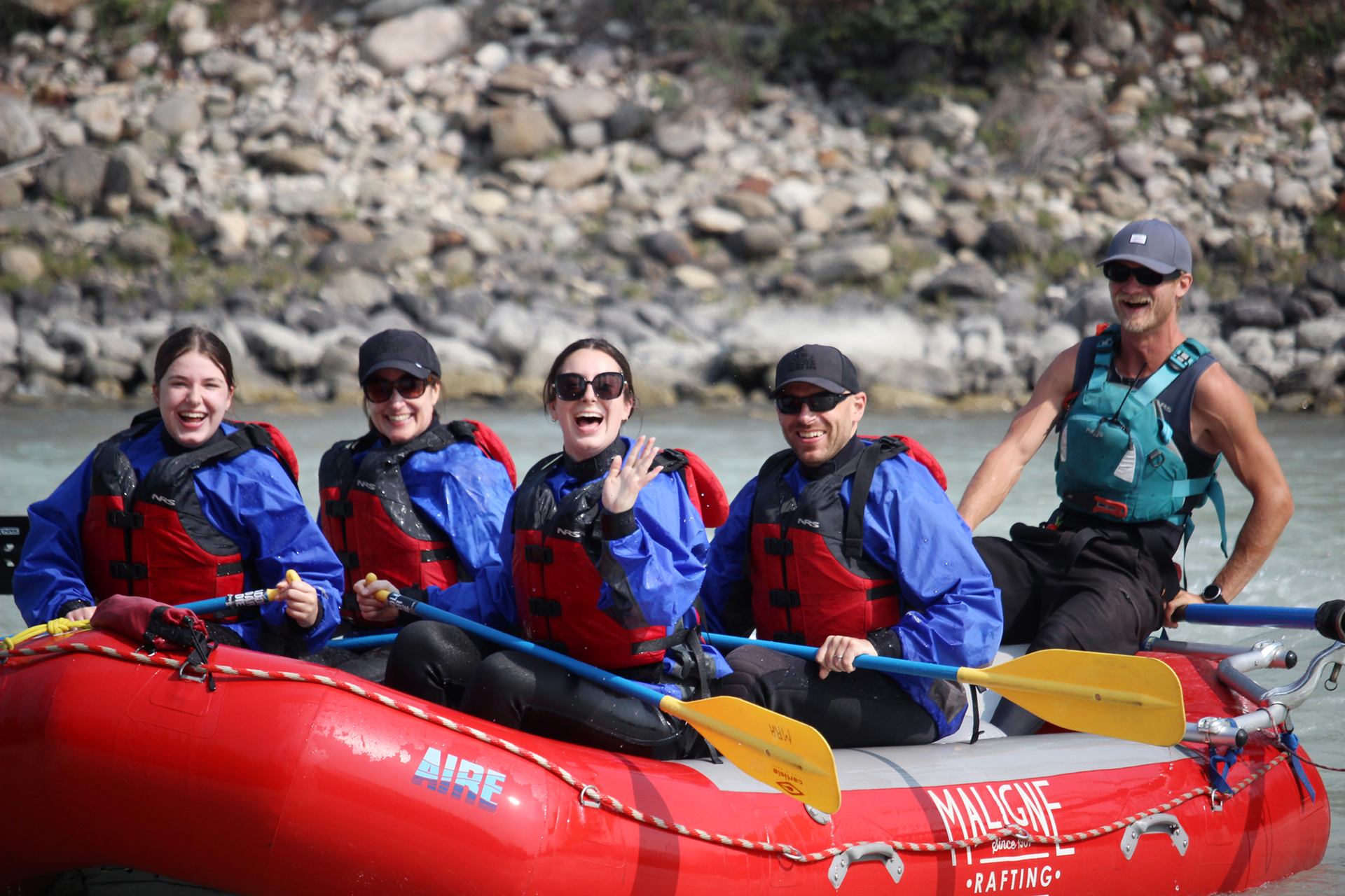 Group sitting in a red raft on calm water, holding paddles as they prepare to begin their river run.