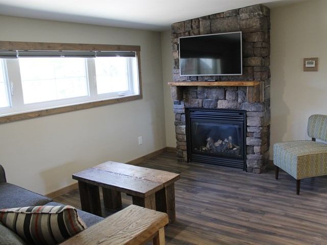 Cozy living room with stone fireplace, mounted TV, rustic furniture, and large window.