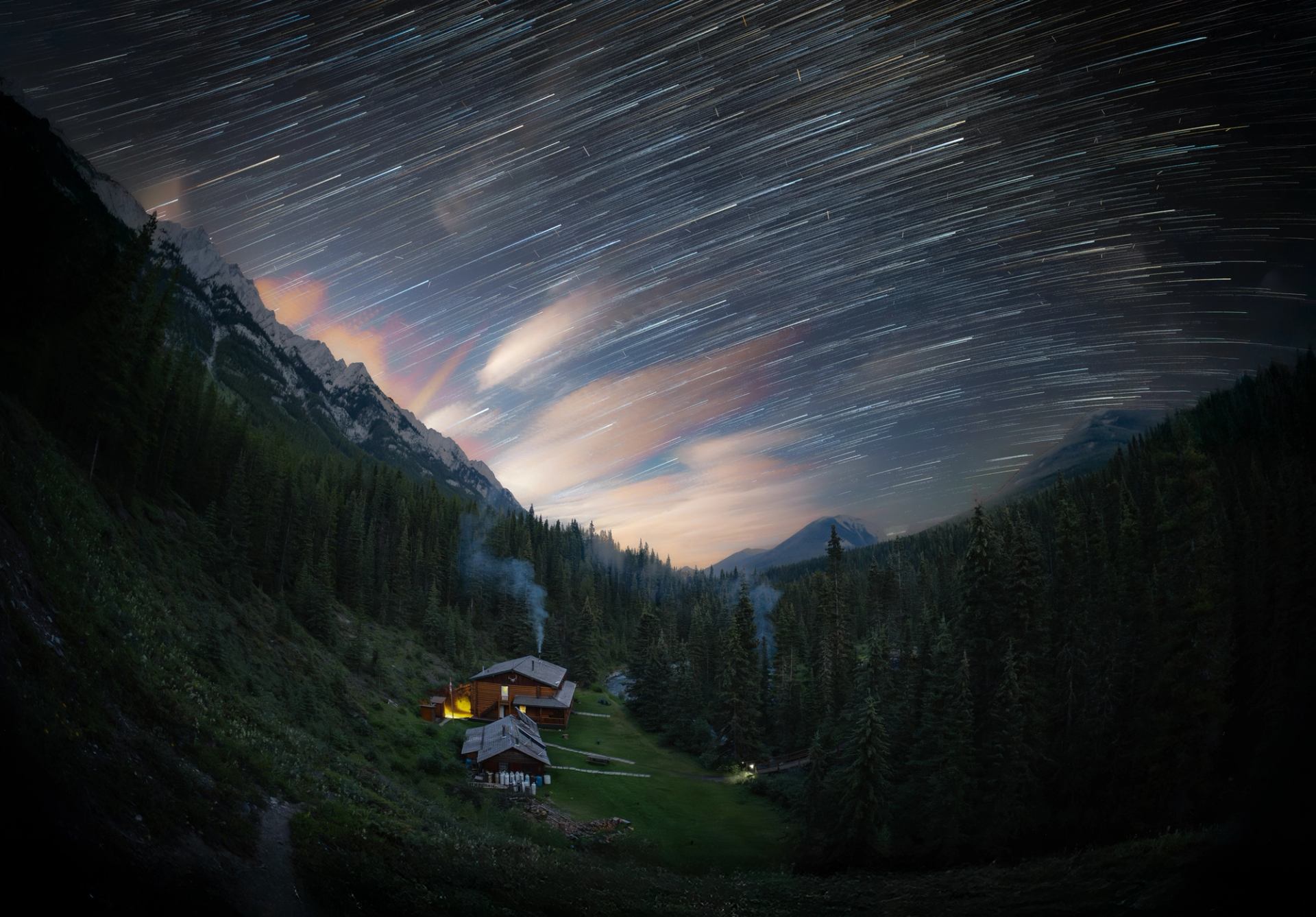 Starry night sky with streaking stars above Sundance Lodge nestled in a forested valley.
