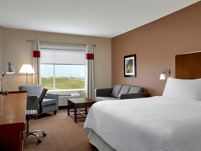 Modern hotel room with bed, sofa, desk, and window view at Four Points Sherwood Park.