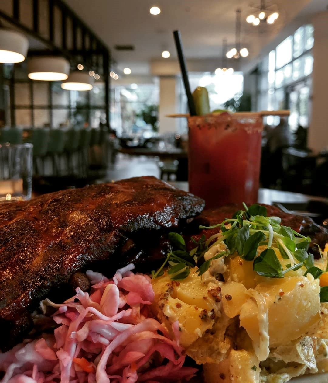 Food plate with ribs and sides in sunlit dining area.