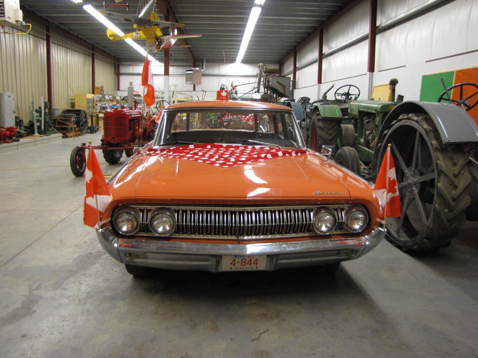 Restored vintage red car displayed indoors alongside tractors and historical equipment.
