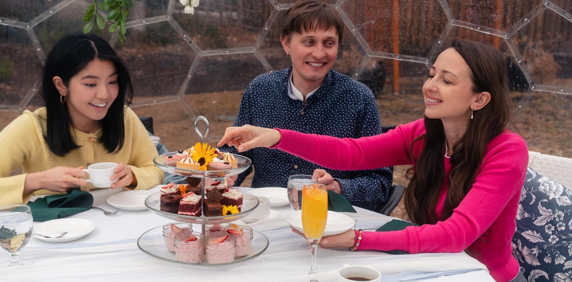 Guests reach for desserts on a tiered stand during a garden dome brunch.
