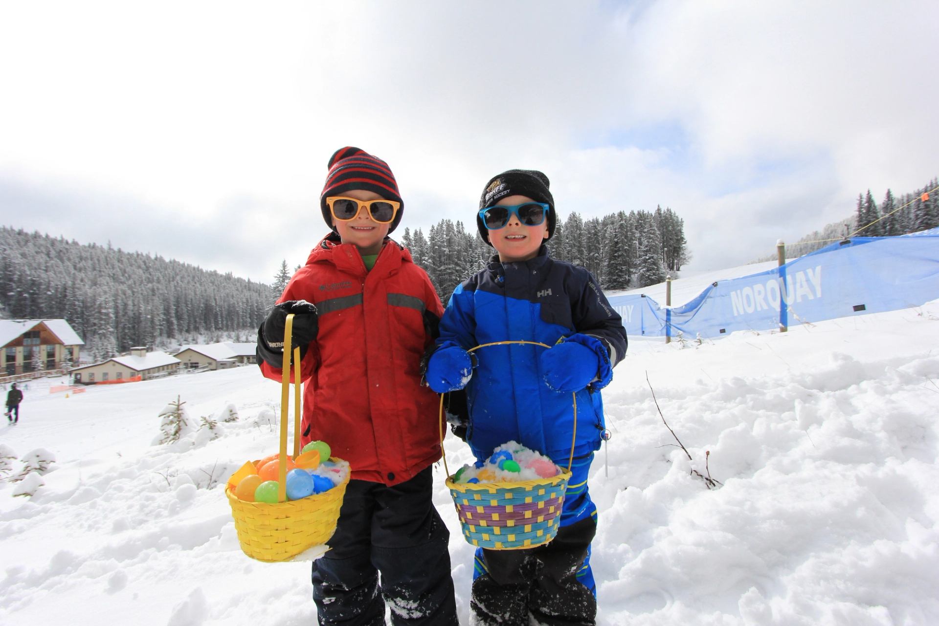 Two kids hold colorful Easter baskets in the snow at Norquay.