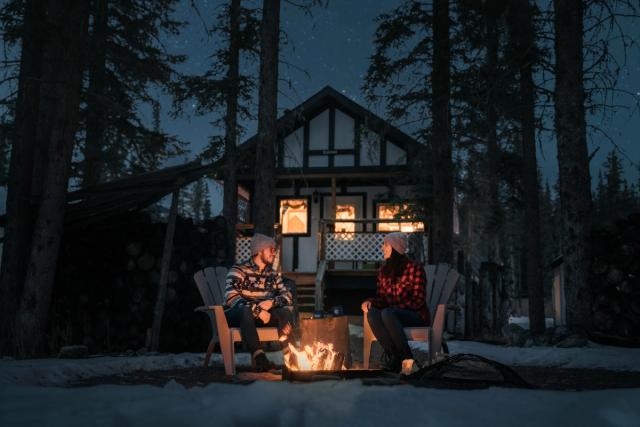 Couple sitting near campfire in front of a cabin at Expanse Cottages.