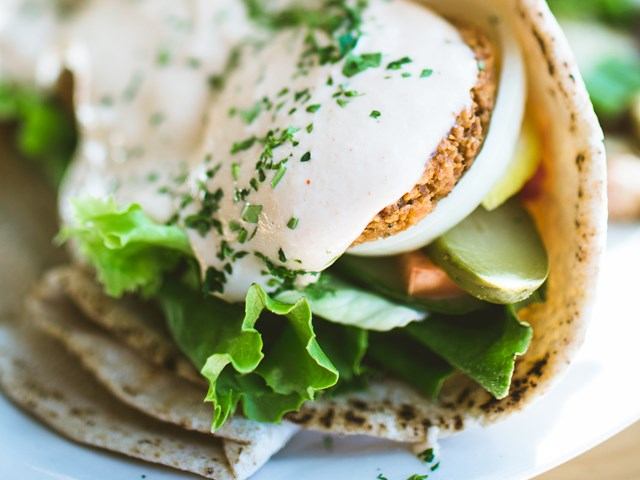 Pita sandwich with falafel, veggies, and herb-topped creamy sauce.