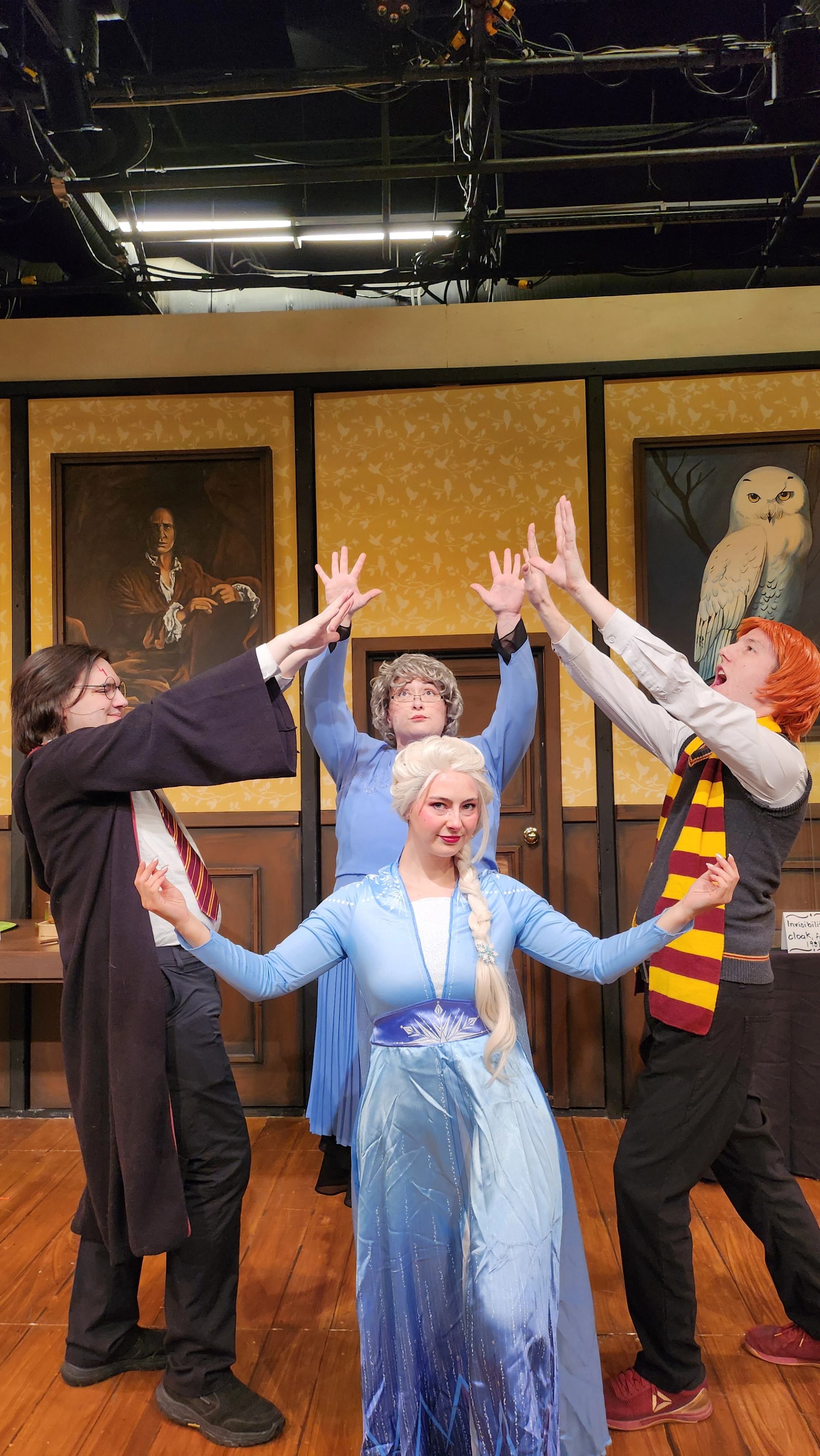 Stage performers in wizard and ice princess costumes pose dramatically in front of paintings.