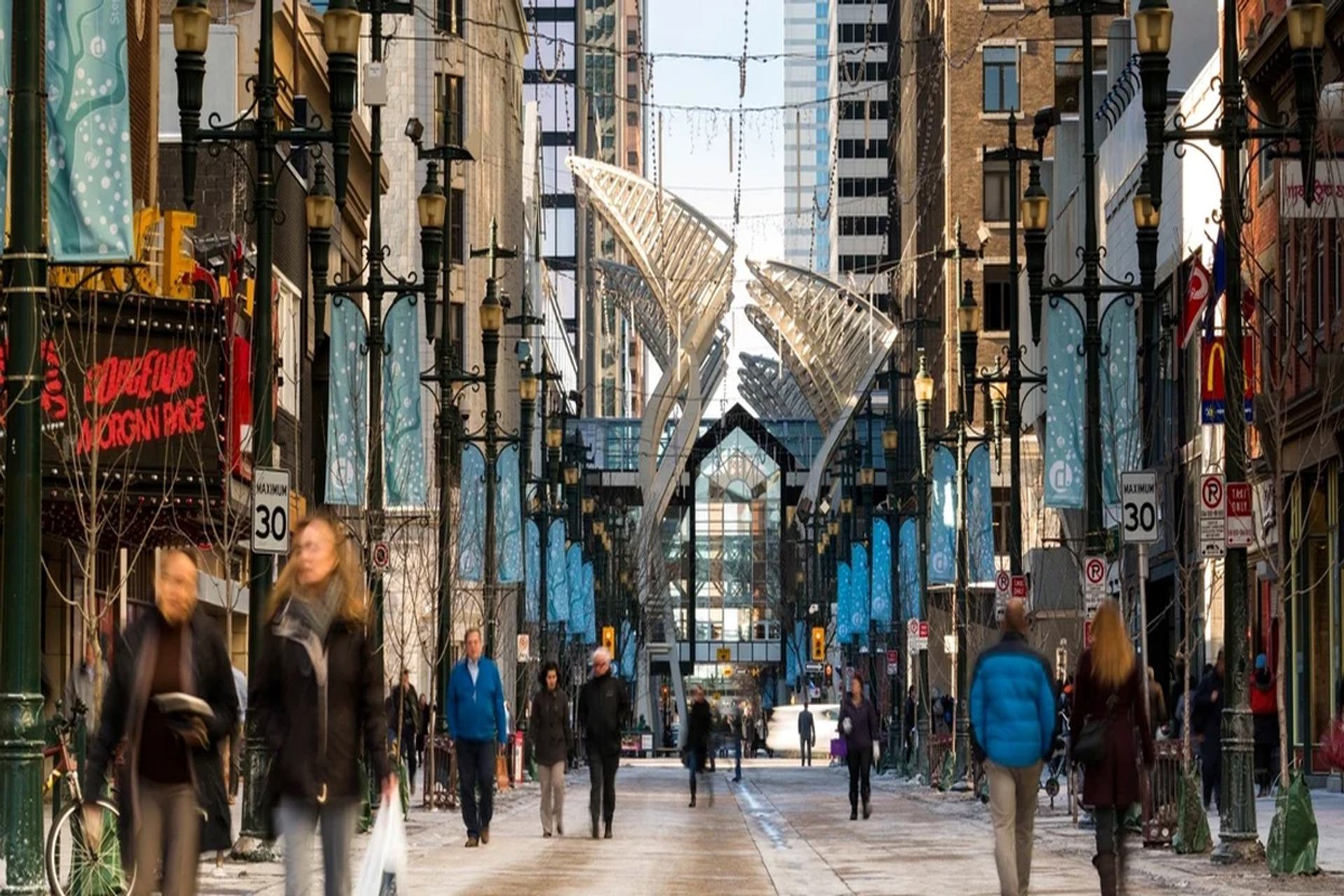 Pedestrians walk along a downtown street lined with buildings, banners and decorative arches.