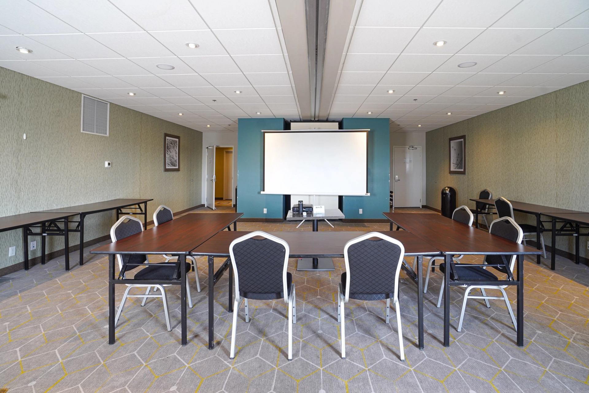 Conference room with projector screen, tables, and chairs against blue and tan walls.