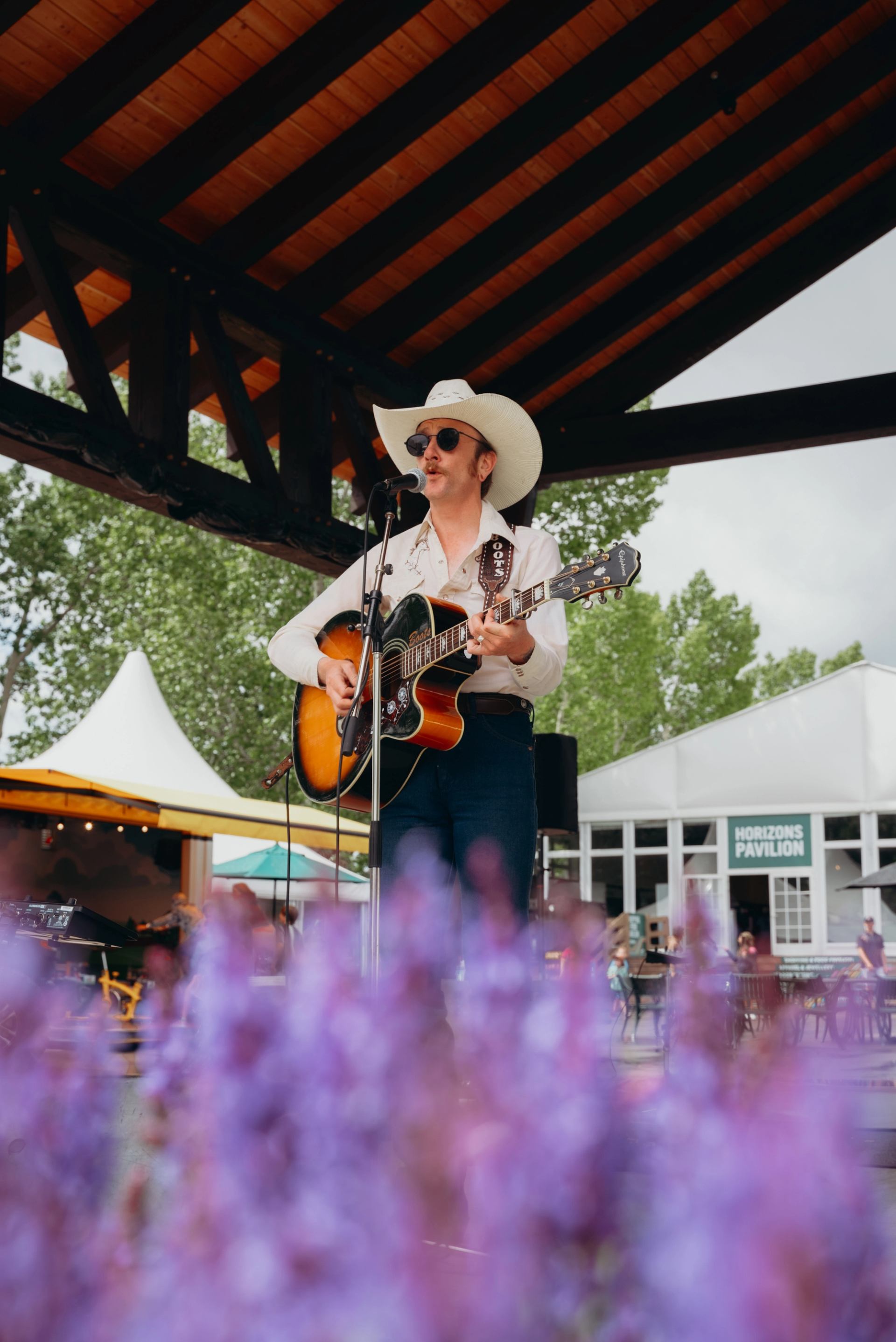 A musician performs onstage with a guitar under a wooden pavilion at the event.