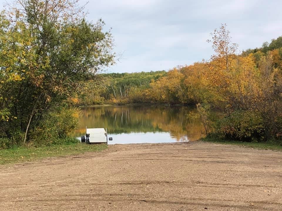 Arm Lake Recreation Area presents a quiet lakeside access point with a small dock extending into still water, surrounded by trees reflecting autumn colors along the shoreline.