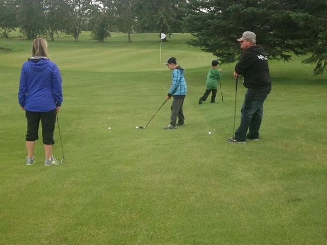 Golfers putt on green near flagstick, with trees in background.