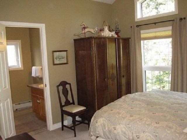 Bedroom with patterned bedspread, wooden armoire, chair, and doorway to bathroom.