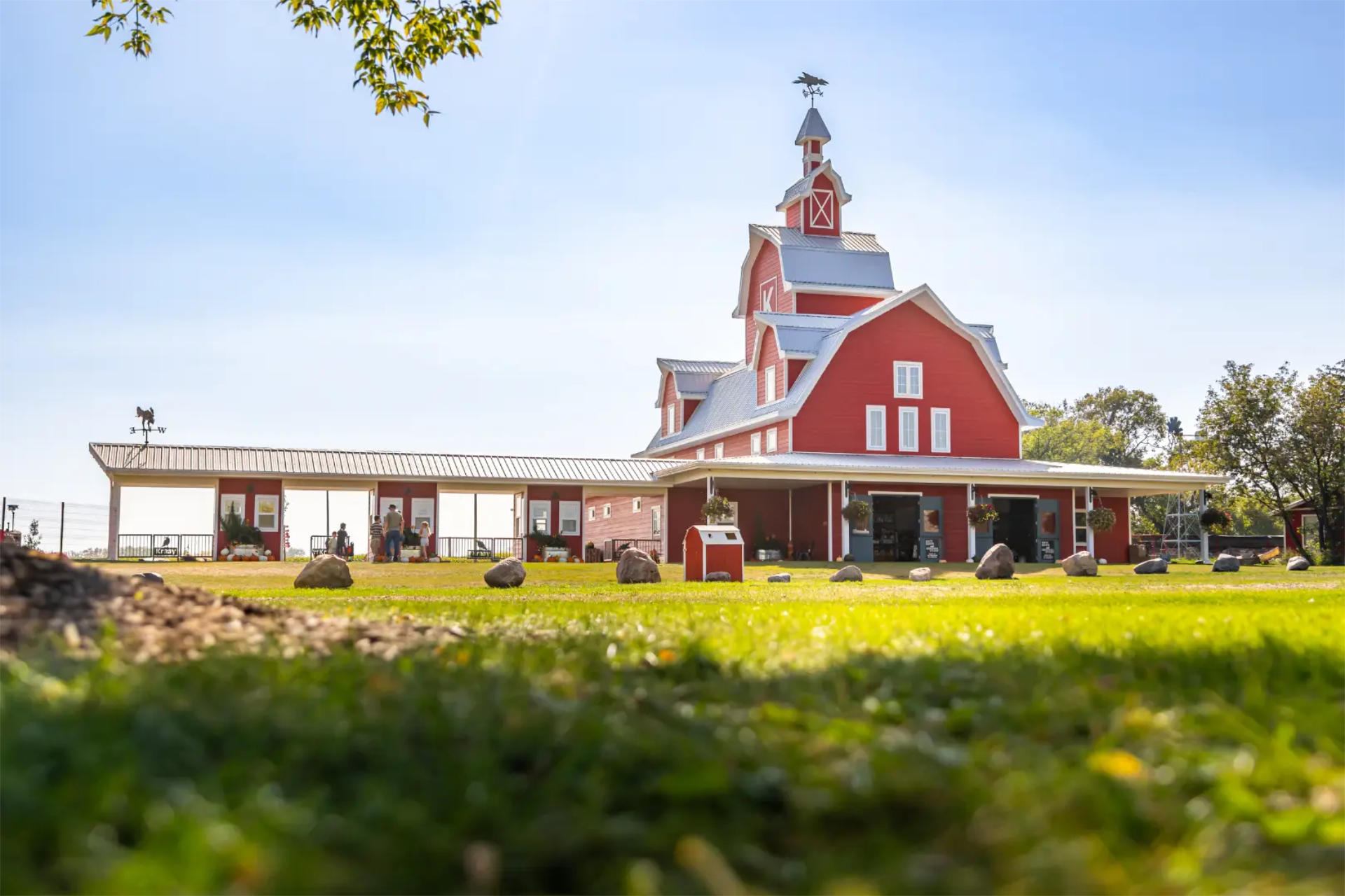 Red barn-style building with tower, green lawn, scattered rocks and distant visitors.
