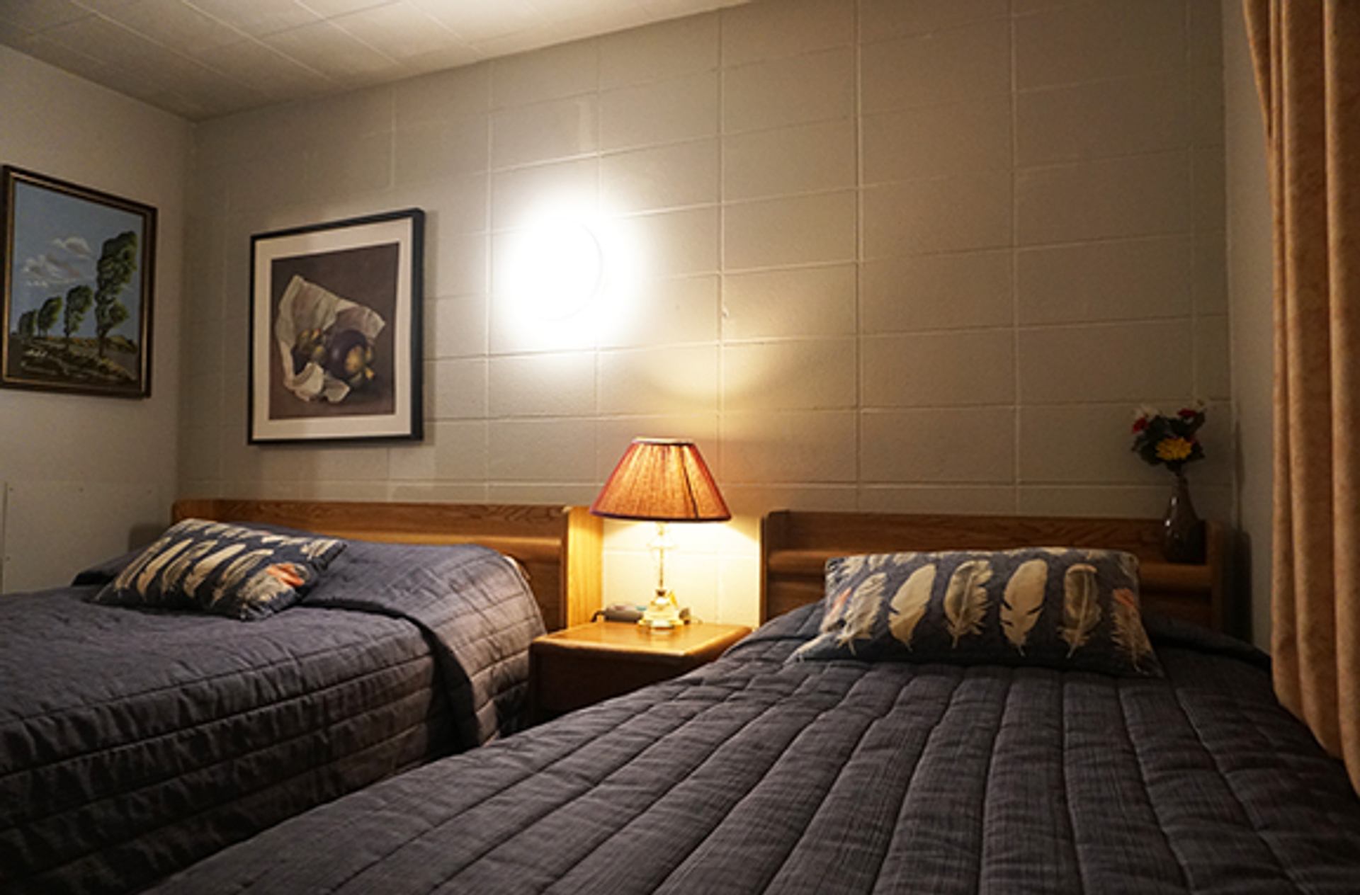 Motel room with two beds, nightstand, lamp, and framed artwork.