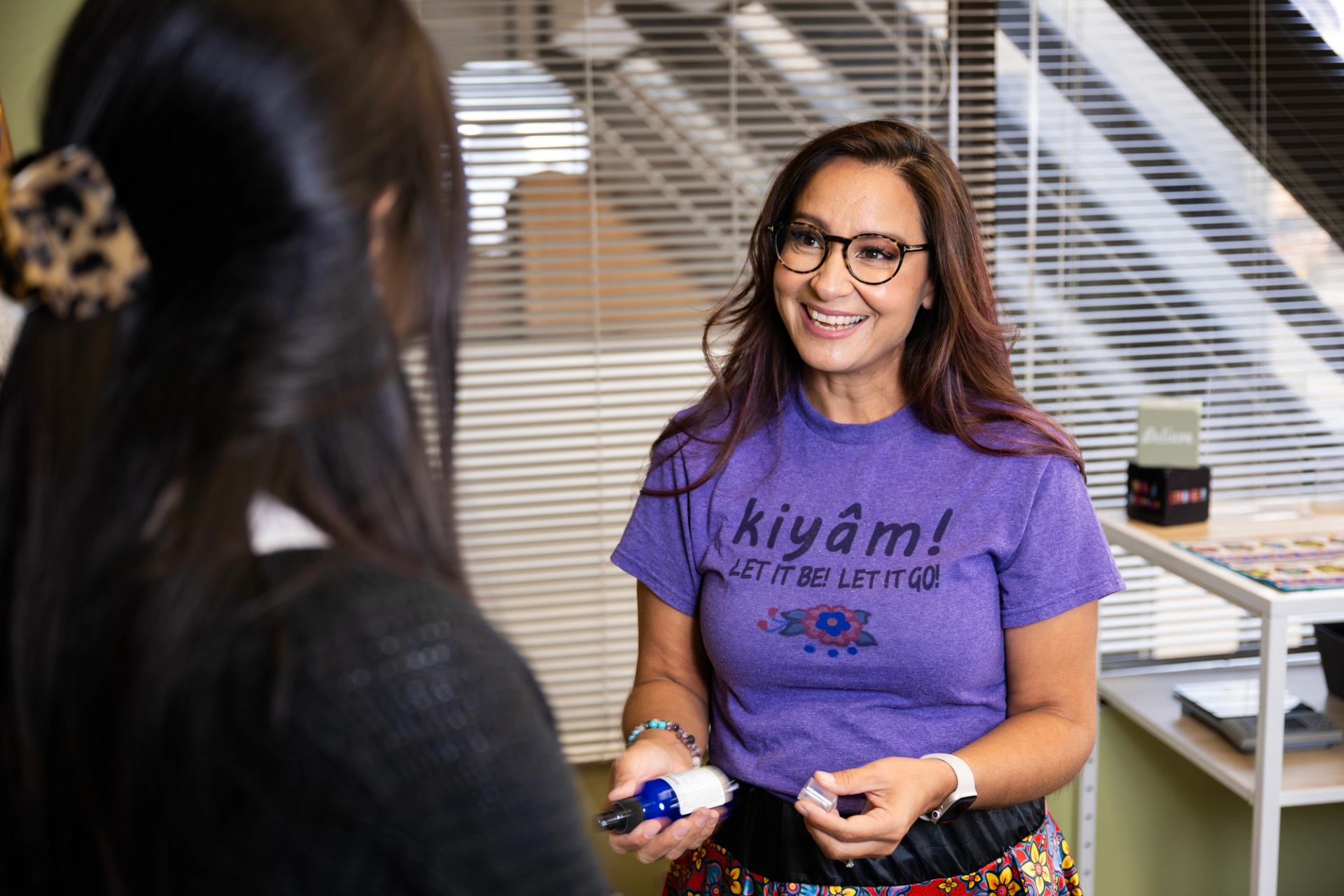 A person indoors offers a wellness bottle while speaking to another person.