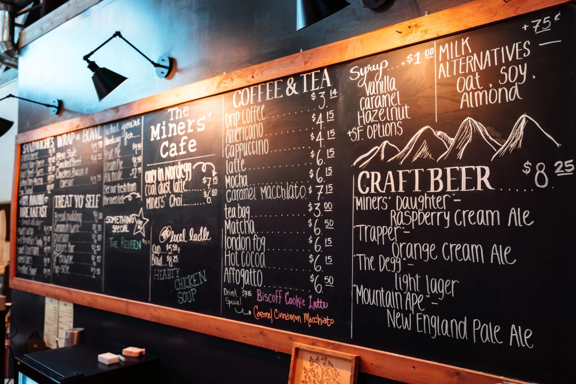 Large chalkboard menu showing coffee, tea, baking, sandwiches and local craft beer offerings.