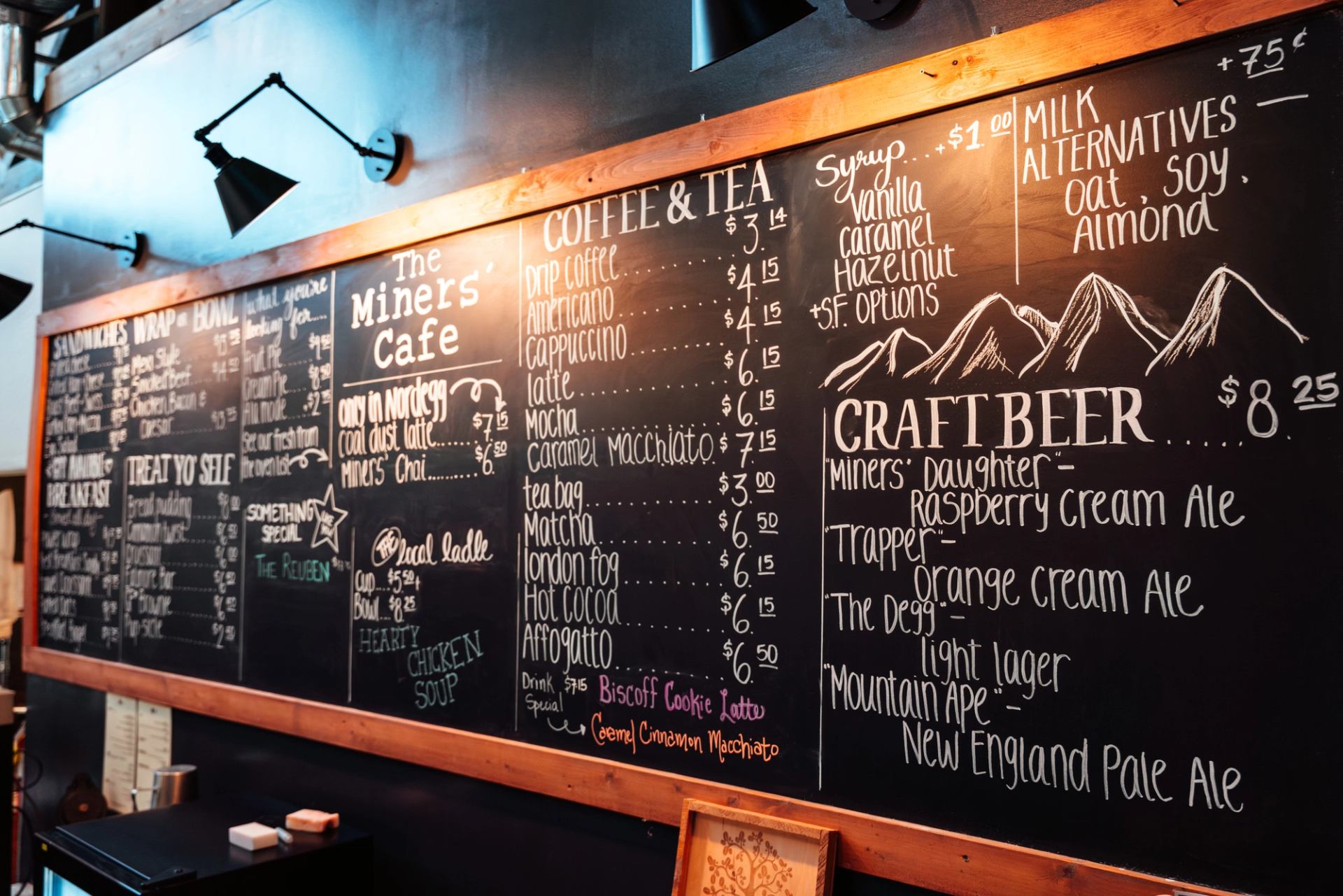 Large chalkboard menu showing coffee, tea, baking, sandwiches and local craft beer offerings.