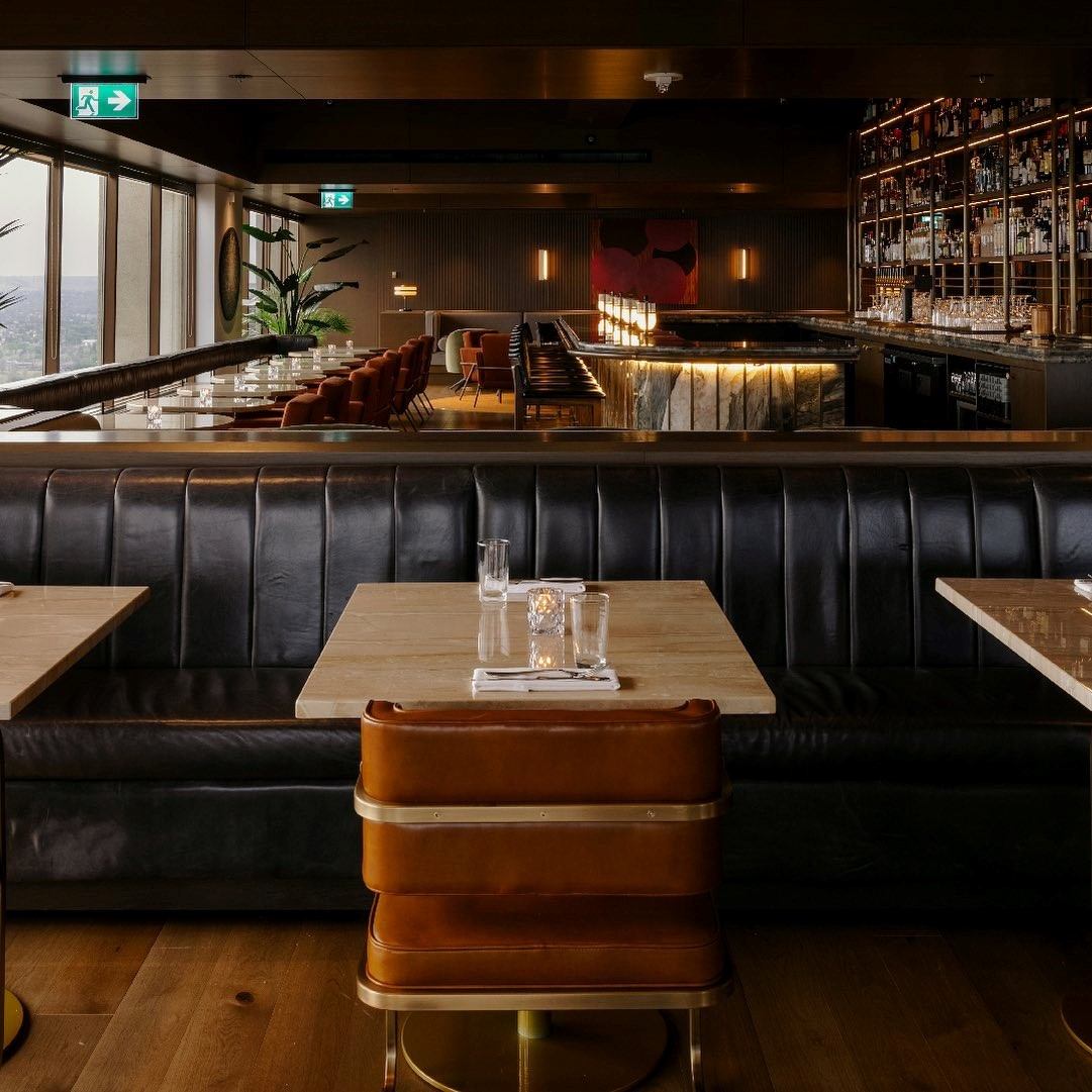 Major Tom restaurant with leather seating, wooden tables, and a well-stocked backlit bar in the background.