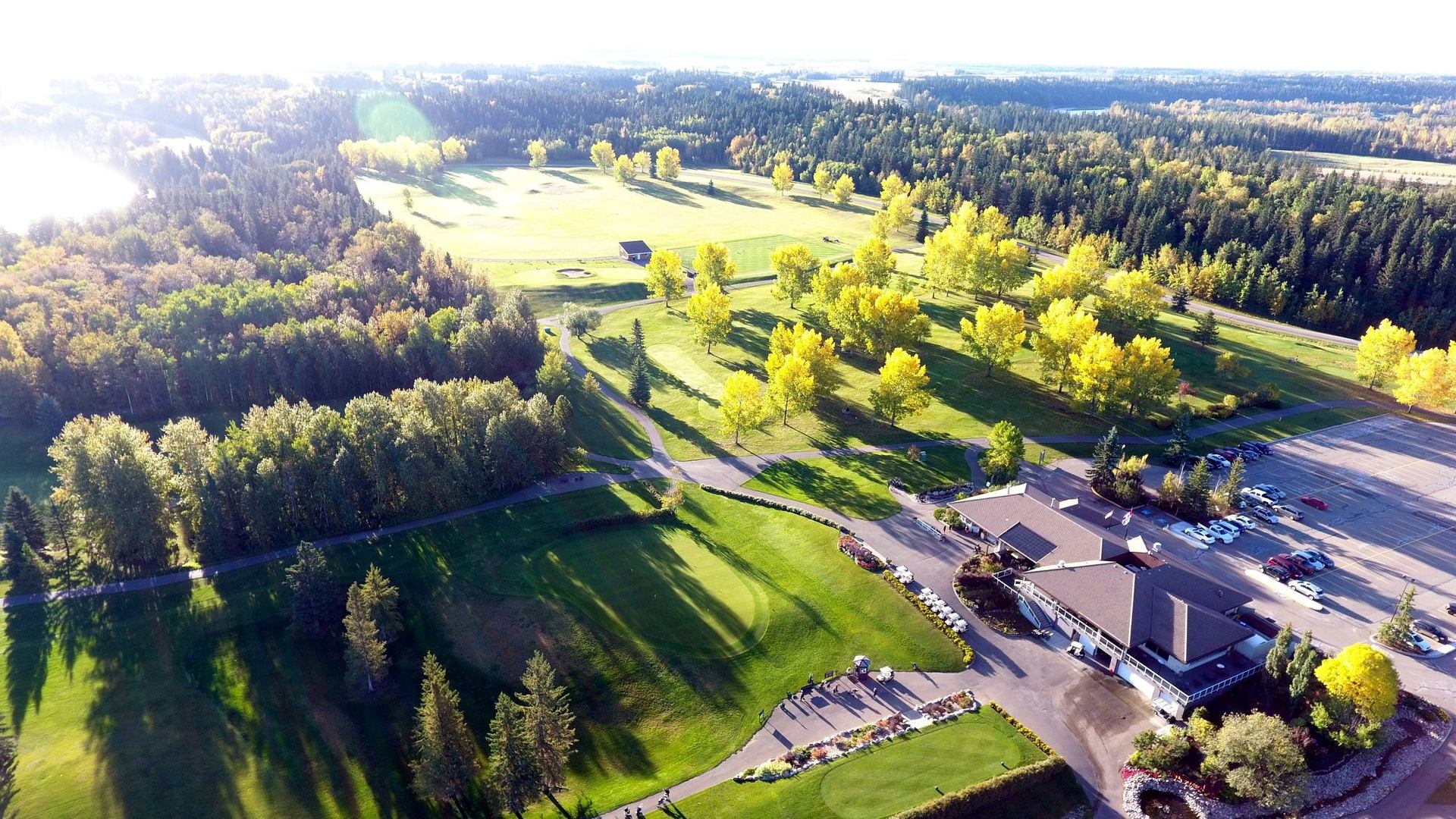 Aerial view of golf course with clubhouse, fairways, and forest.