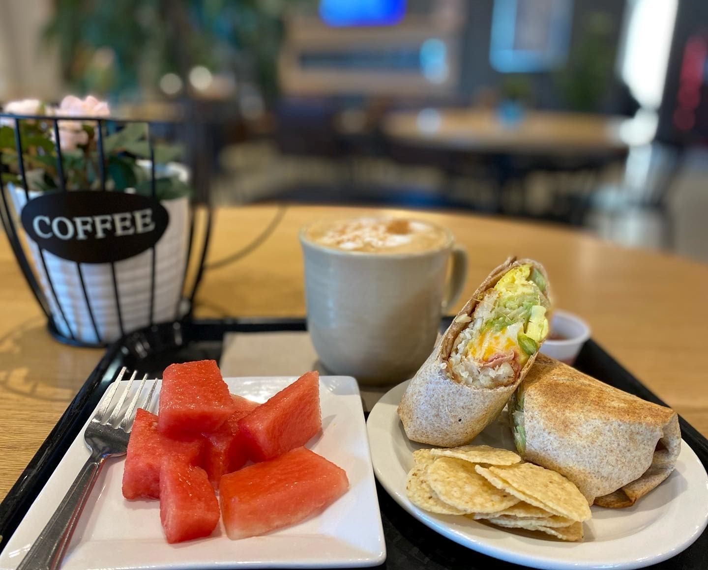 Wrap sandwich, chips, watermelon, and coffee on a cozy café table.