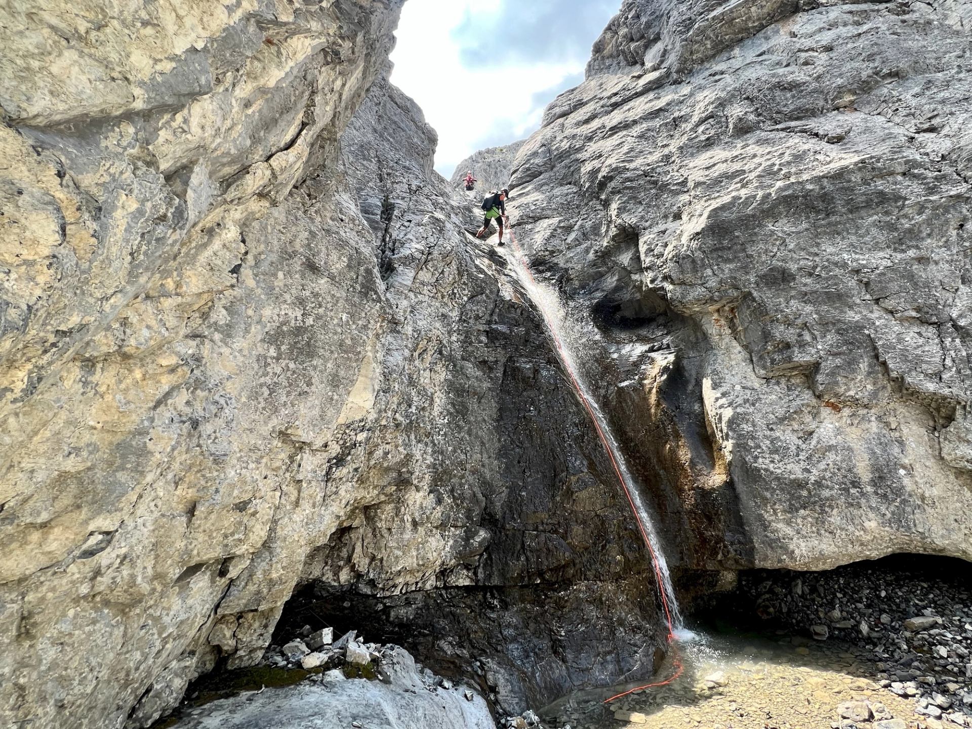Person rappelling down a steep canyon wall beside a small waterfall.