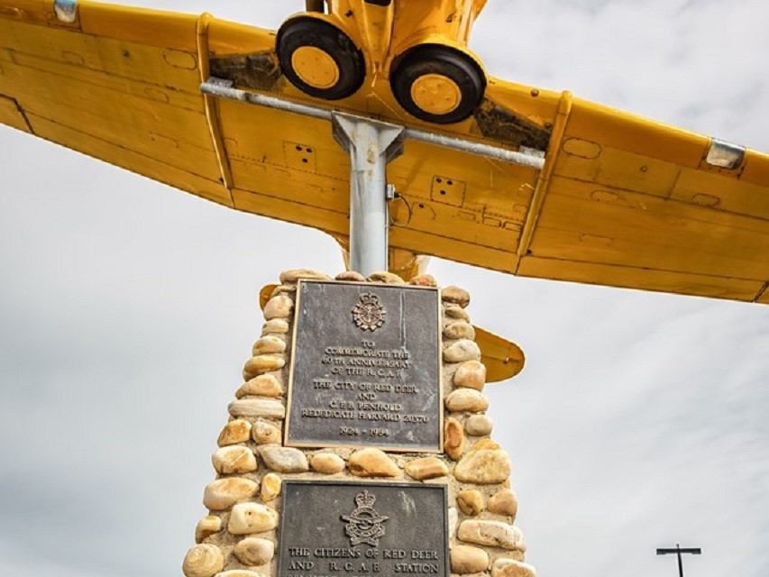 Yellow plane atop stone monument with plaques honoring WWII air training at Red Deer Regional Airport.