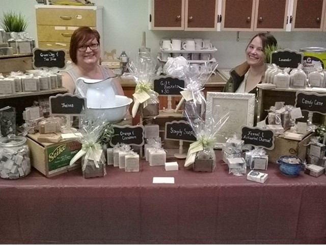 Farmers market table display with boxed soaps and two vendors at Town and Country Farmers’ Market.