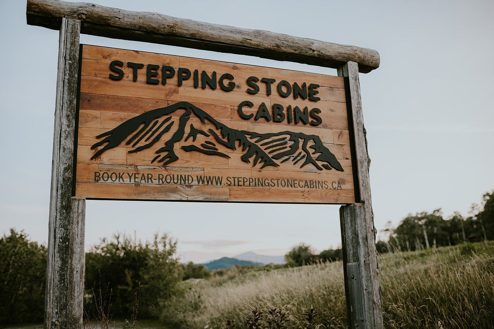Wooden Stepping Stone Cabins sign stands beside a grassy field with distant mountains.