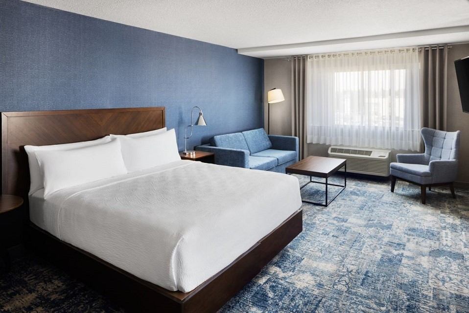 Modern hotel room with bed, blue sofa, and accent wall at Four Points by Sheraton.