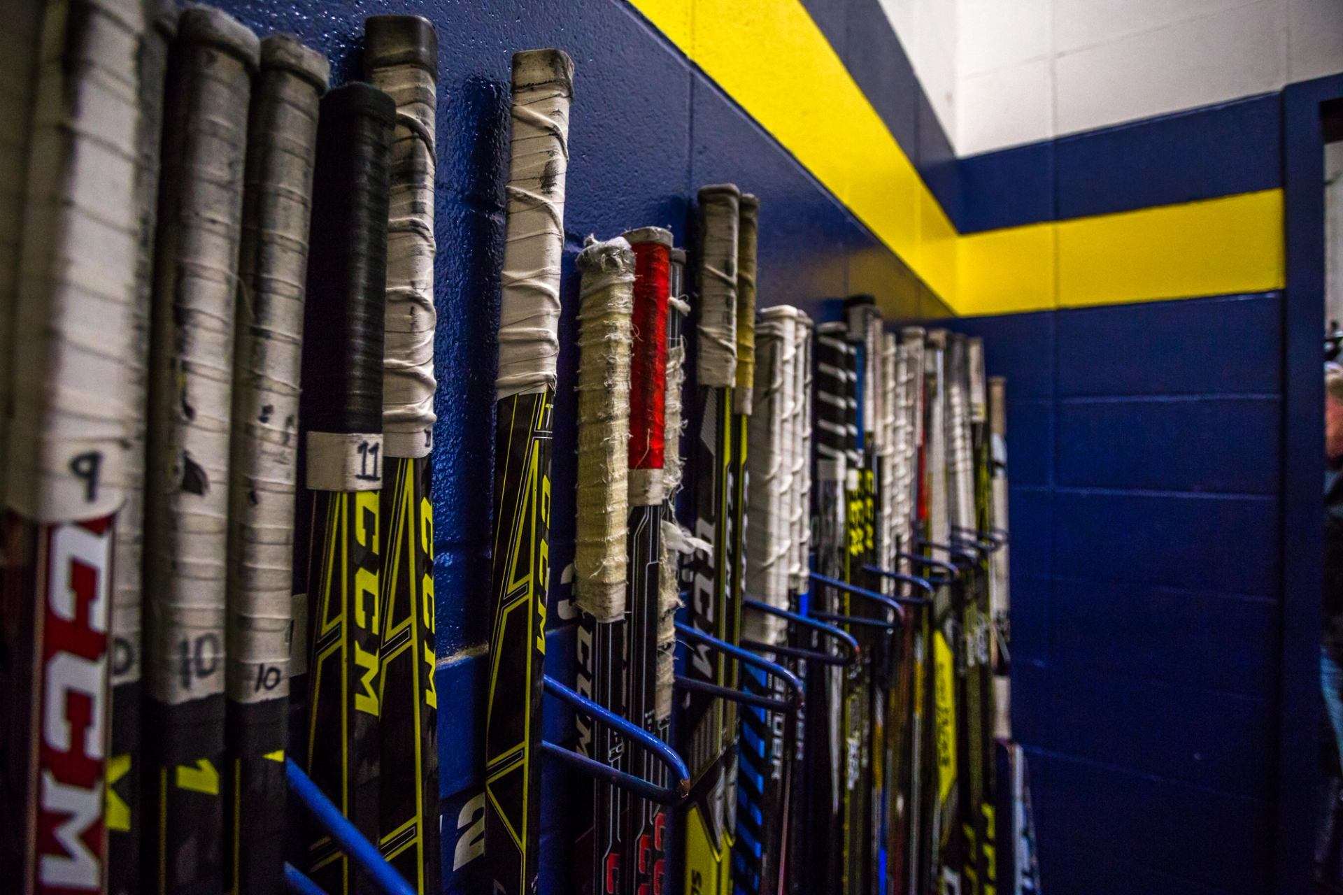 Row of taped hockey sticks lined up against a blue and yellow wall.