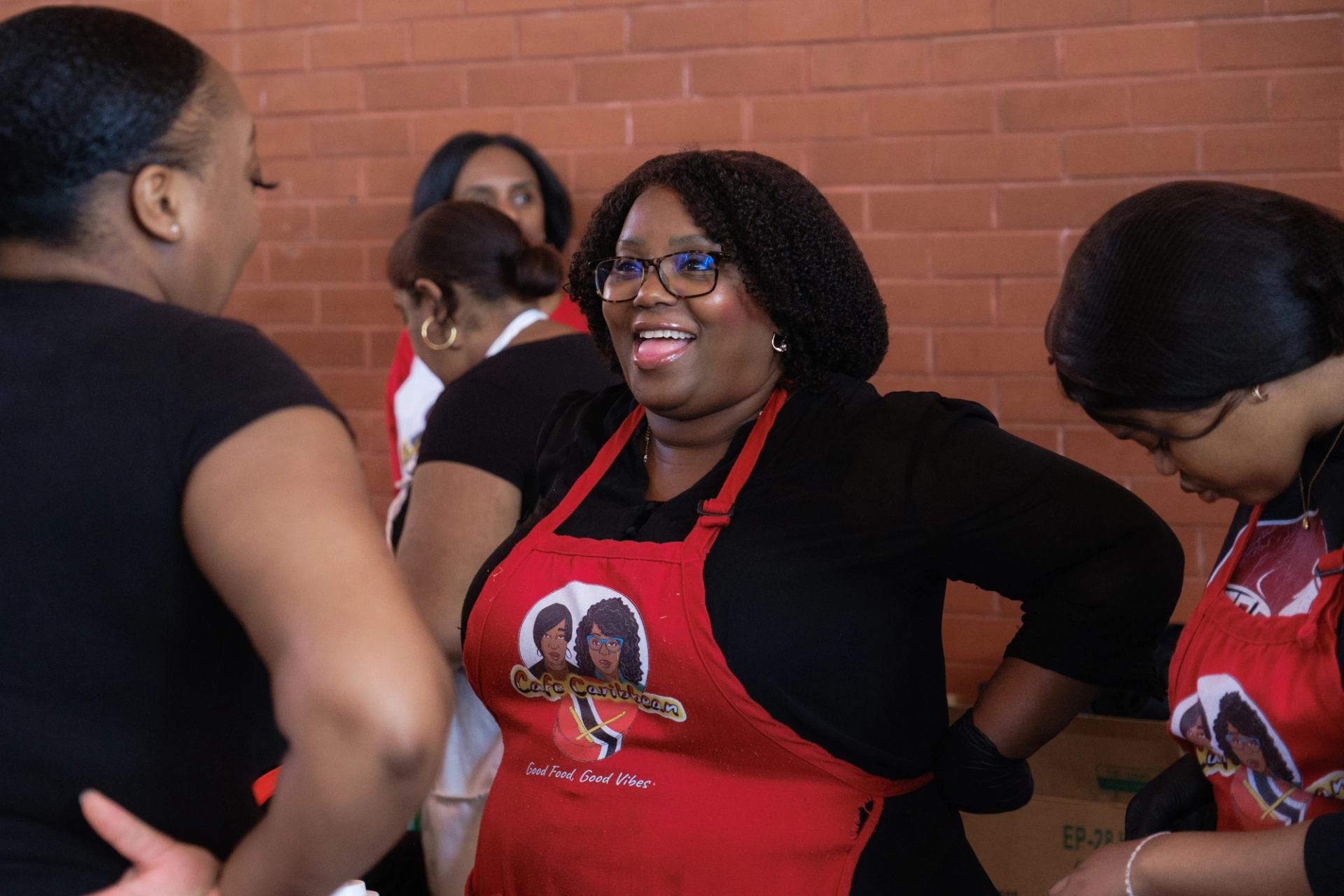 People wearing Cafe Caribbean aprons stand and talk in front of a brick wall.