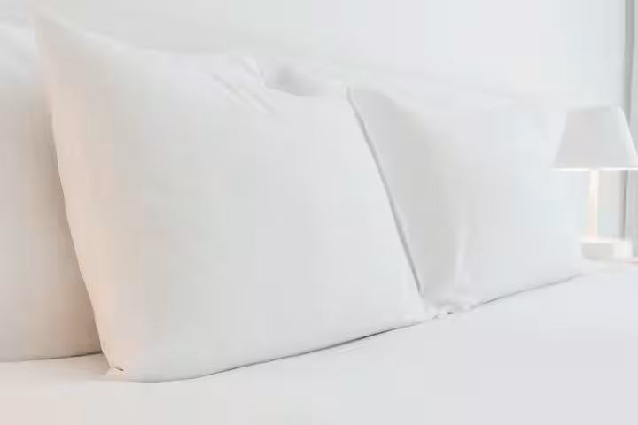 Neatly arranged white pillows and crisp bedding in a clean, bright hotel room