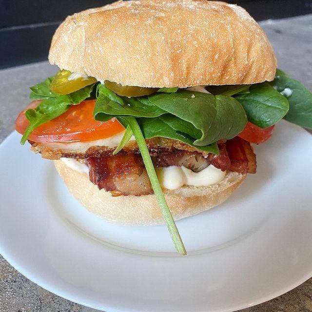 Fresh sandwich with bacon, spinach, tomato, and pickles on a toasted bun.