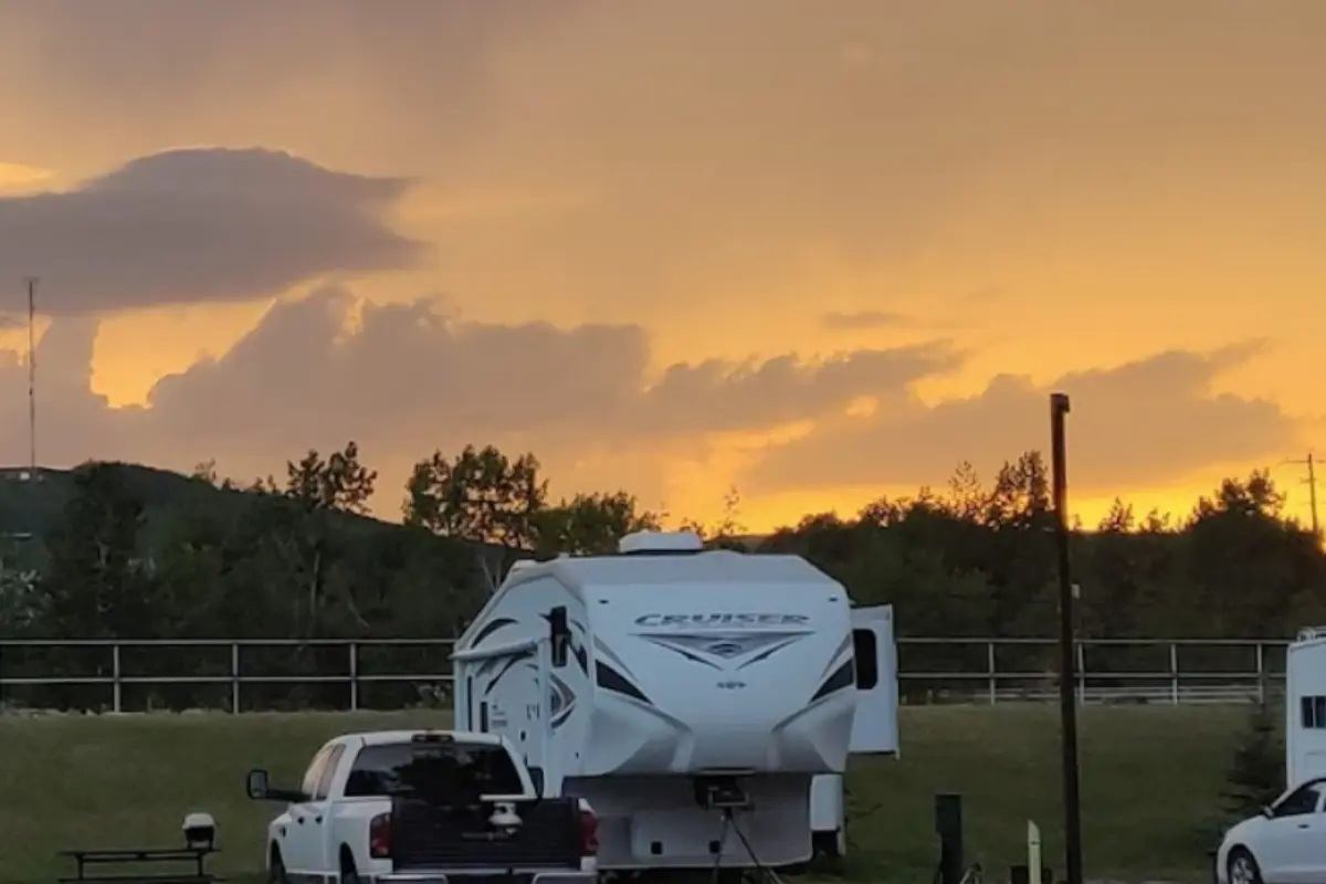 Recreational vehicle and pickup truck parked on grassy campsite under orange sunset sky.