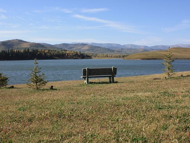 A bench facing a calm lake with hills and trees in the distance.