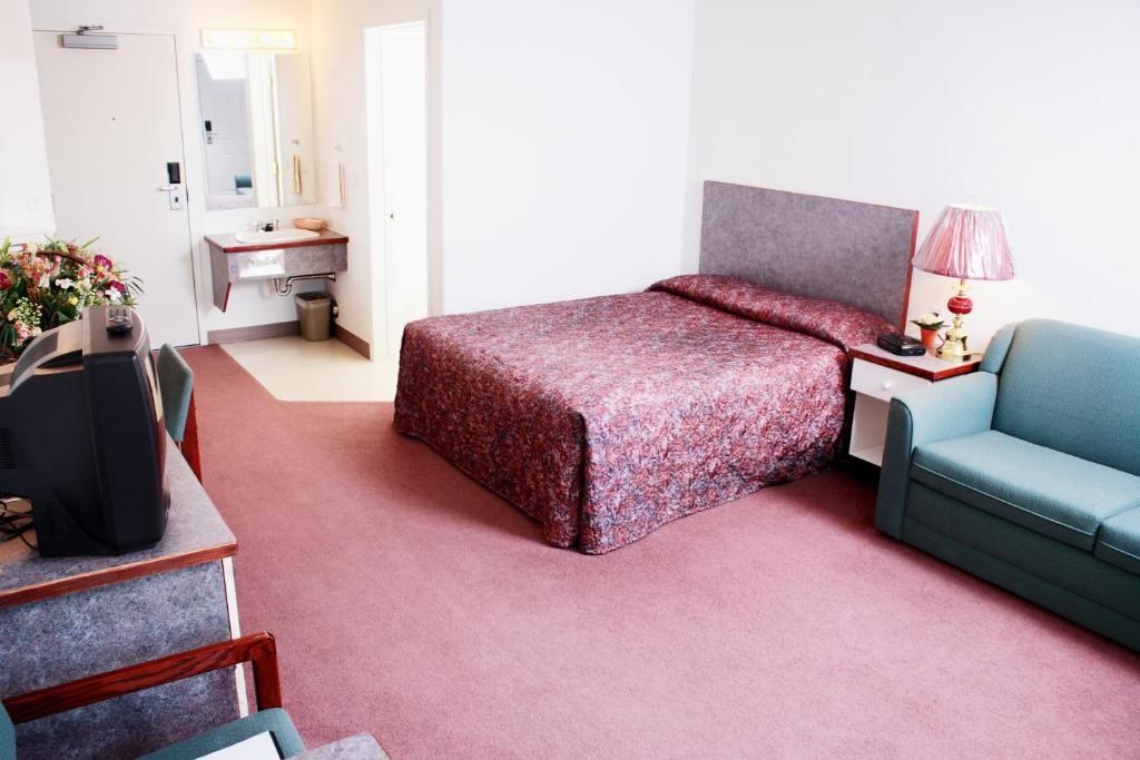 Hotel room with red bedspread, green sofa, TV, and vanity area in background.
