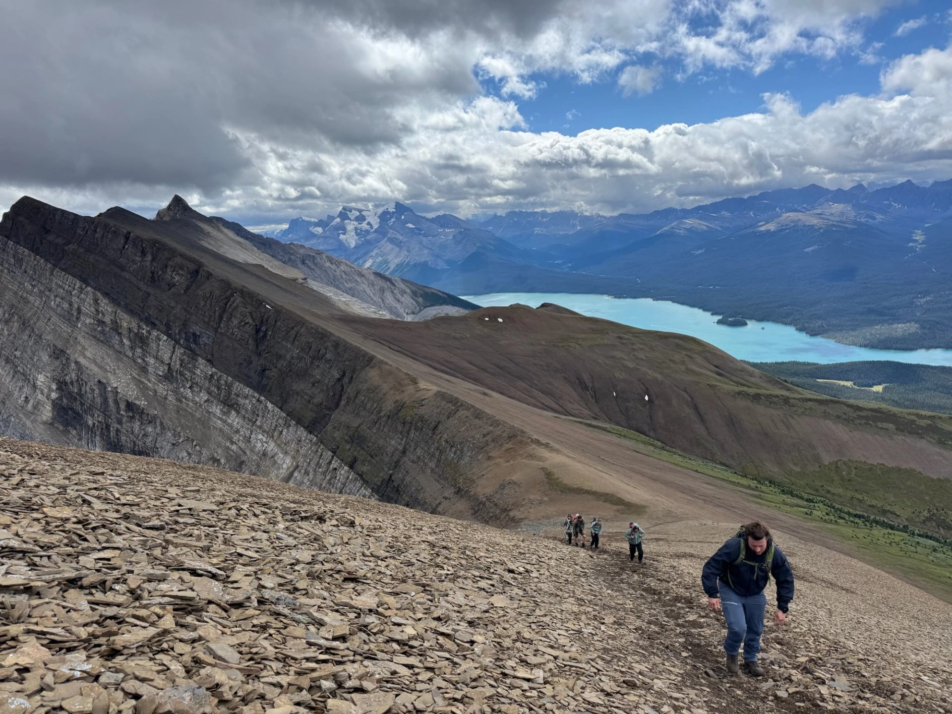 hiking group making their way up shale covered slope overlooking mountain lake.