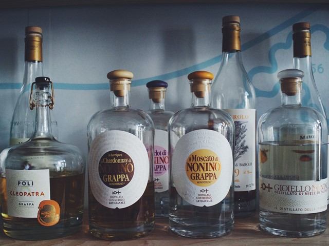 Assorted grappa bottles with cork stoppers lined up on a wooden shelf.