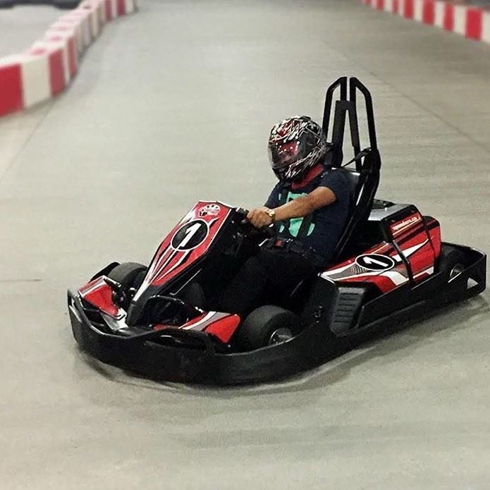 Racer in red and black go-kart turning on indoor track with safety barriers.