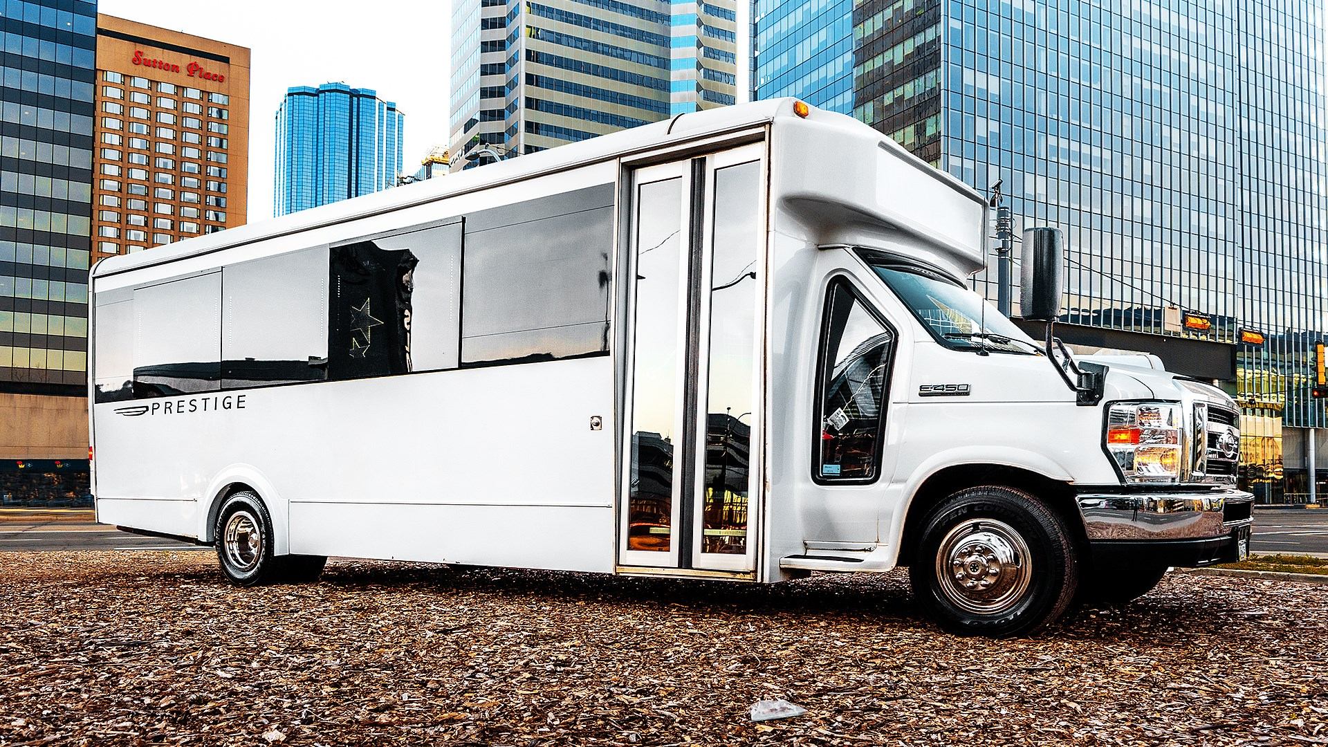 Prestige Limousine white shuttle bus parked in a downtown area with tall glass buildings.