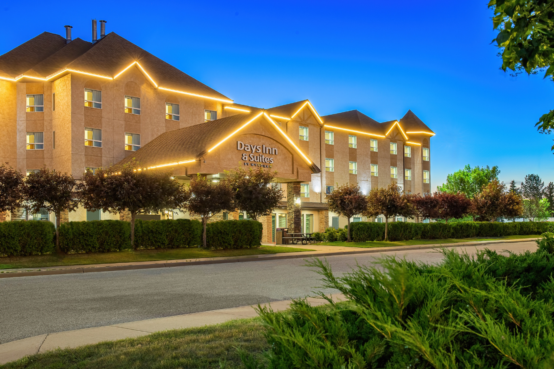 exterior photo of the hotel at dusk, the hotel is lit up with white rope lighting around the roof