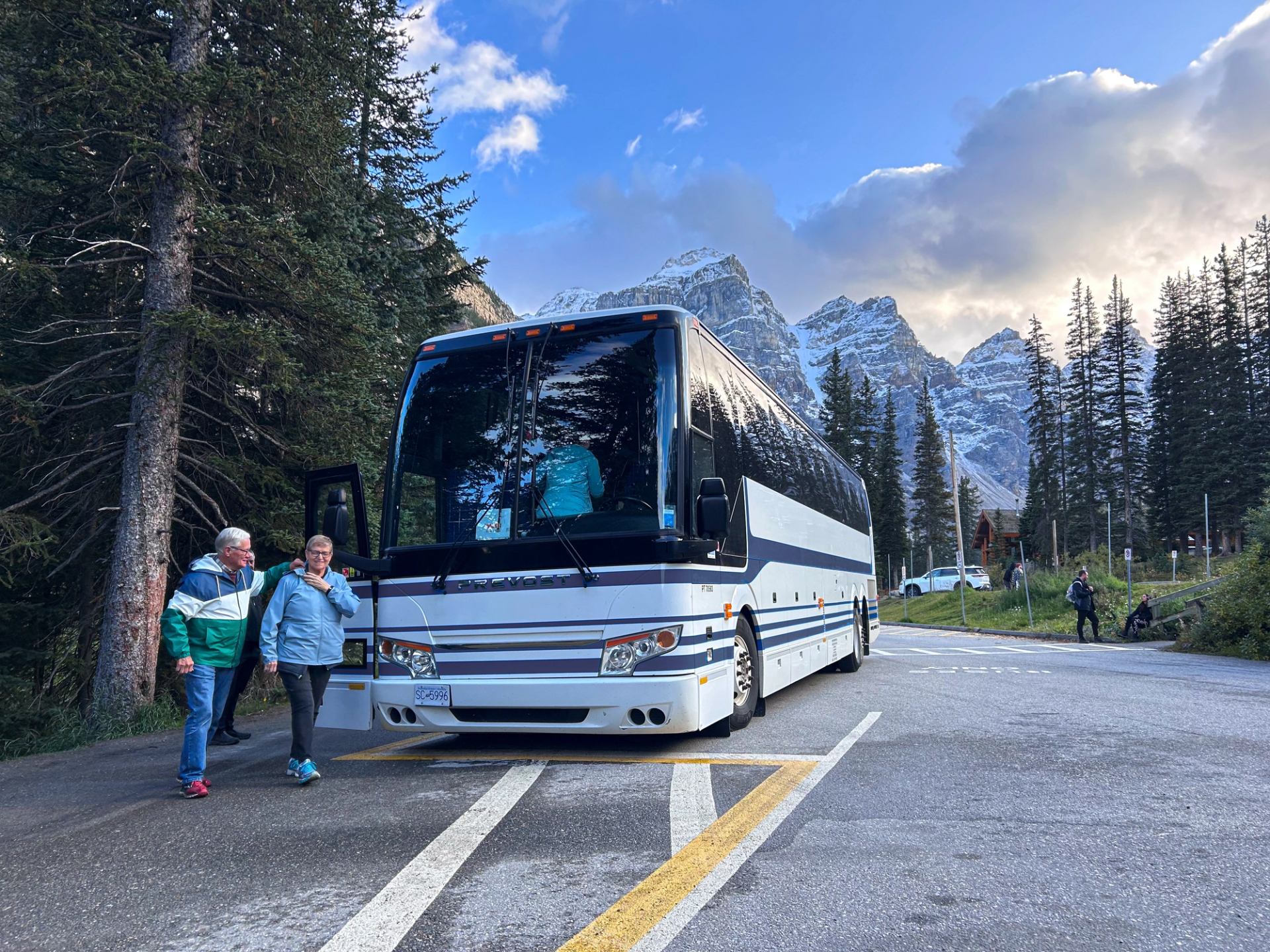 A tour bus parked on a mountain road with two people walking nearby.