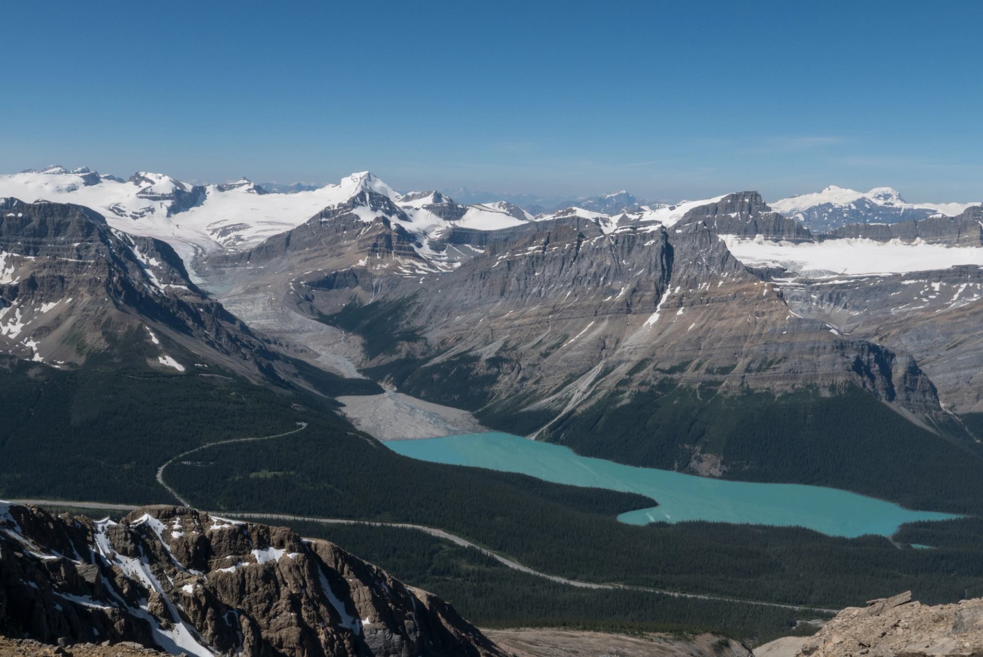 Turquoise lake surrounded by rugged, snow‑capped mountains viewed from above.