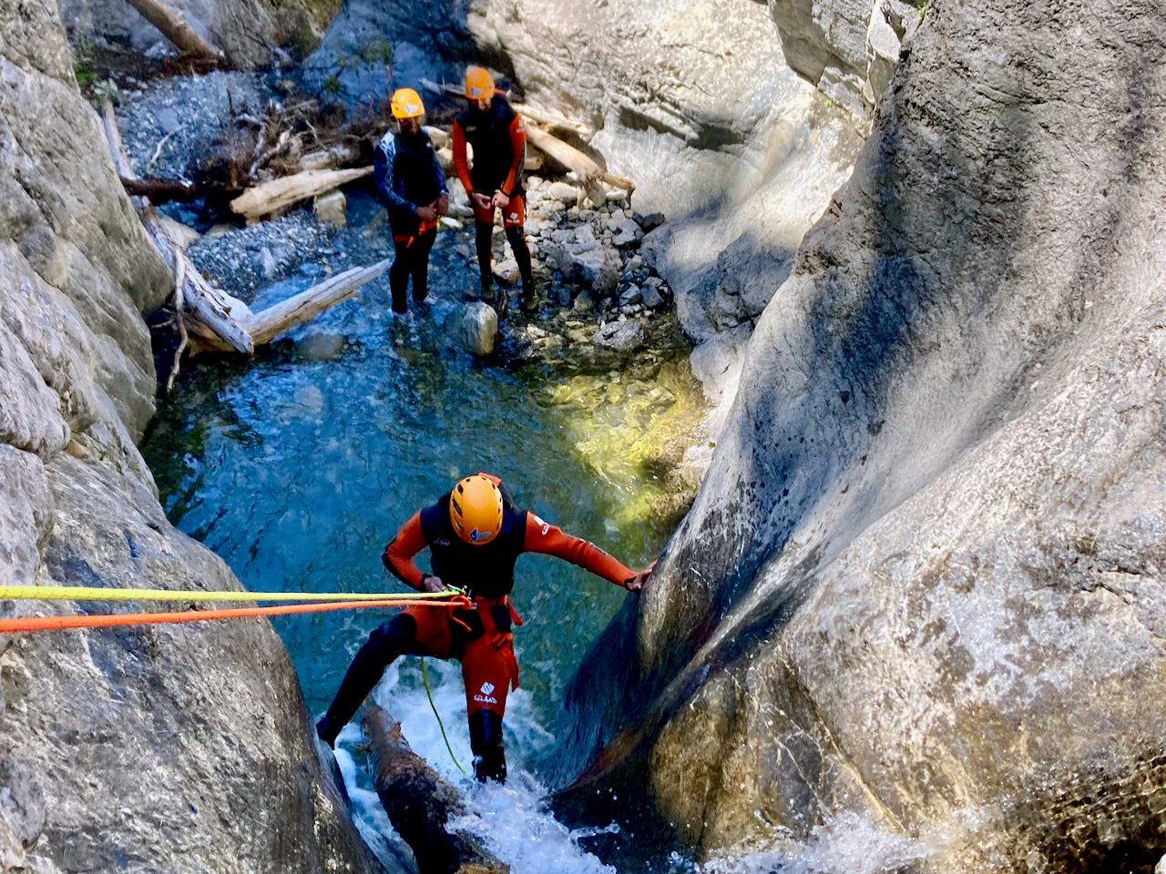 Two people canyoning through a narrow gorge with ropes and clear water.